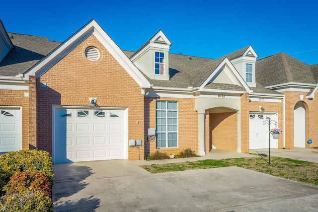 view of front of house featuring a shingled roof, concrete driveway, brick siding, and an attached garage