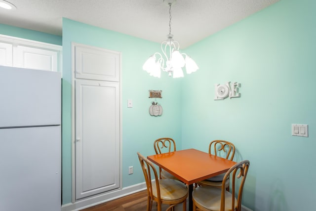 dining room featuring a textured ceiling, baseboards, dark wood-style flooring, and a notable chandelier