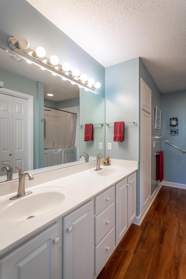 bathroom with a textured ceiling, separate washer and dryer, a sink, and wood finished floors