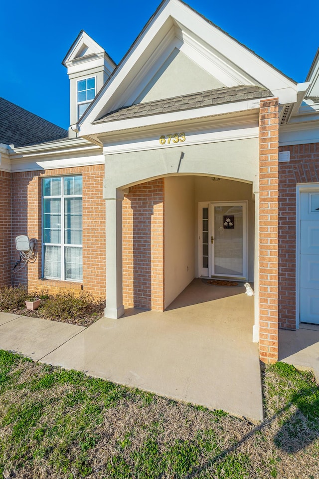 property entrance with brick siding, roof with shingles, and stucco siding