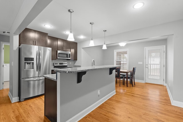 kitchen with dark brown cabinetry, light wood finished floors, appliances with stainless steel finishes, a breakfast bar area, and hanging light fixtures