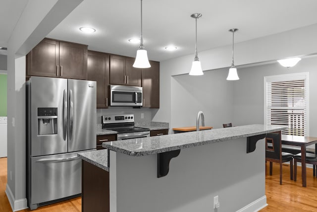 kitchen featuring stainless steel appliances, dark brown cabinets, light wood-style flooring, and a kitchen bar