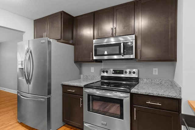 kitchen featuring light wood finished floors, light stone counters, appliances with stainless steel finishes, and dark brown cabinetry