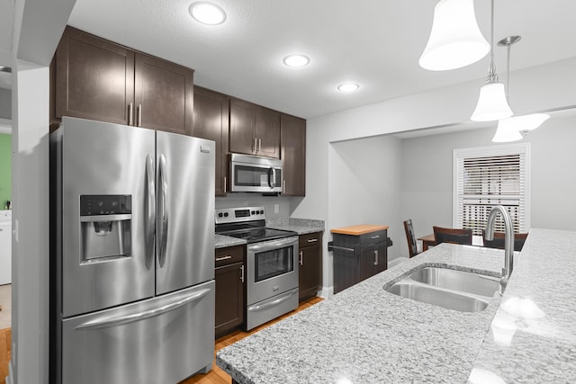 kitchen featuring pendant lighting, light wood finished floors, appliances with stainless steel finishes, a sink, and dark brown cabinetry