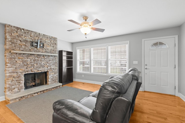 living room featuring light wood-style flooring, a fireplace, baseboards, and ceiling fan