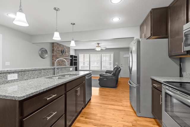 kitchen with stainless steel appliances, light wood-style floors, open floor plan, a sink, and dark brown cabinetry