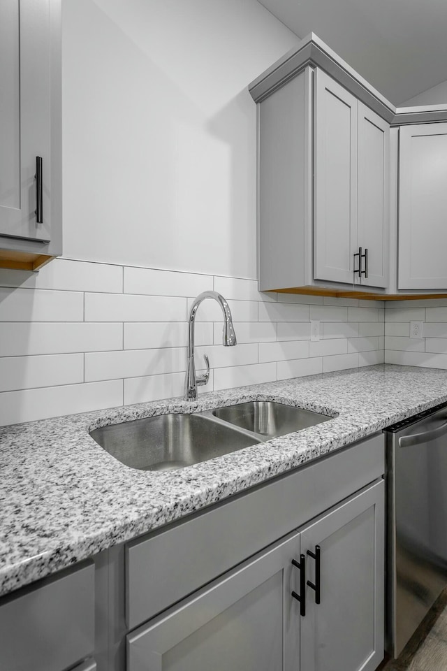 kitchen featuring gray cabinets, a sink, backsplash, and stainless steel dishwasher