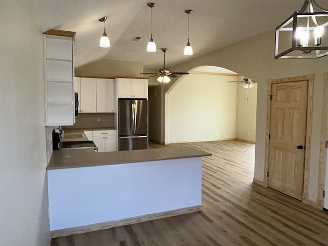 kitchen featuring arched walkways, a peninsula, wood finished floors, white cabinets, and freestanding refrigerator