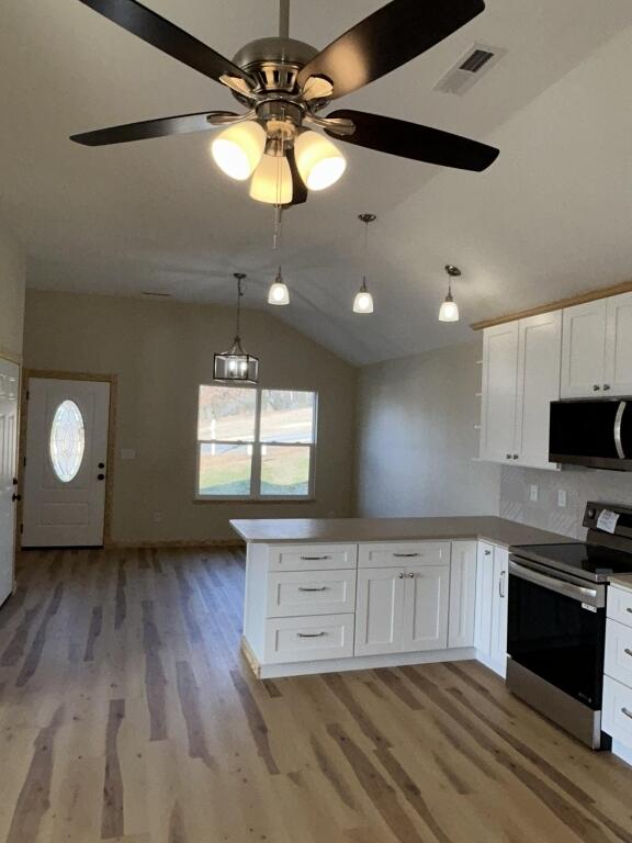 kitchen featuring stainless steel appliances, lofted ceiling, visible vents, white cabinets, and a peninsula