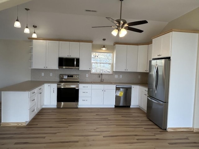 kitchen with stainless steel appliances, lofted ceiling, visible vents, white cabinetry, and a sink