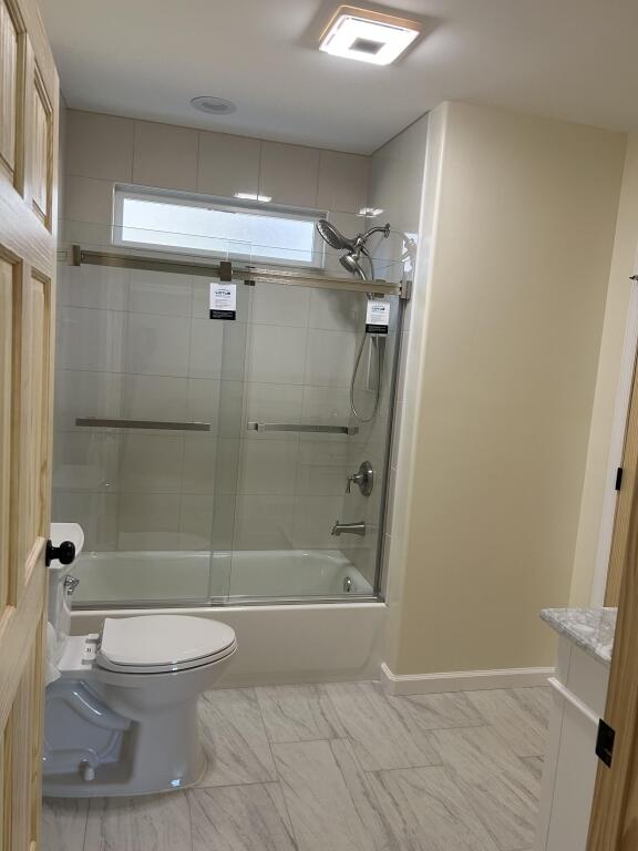 full bath featuring marble finish floor, shower / bath combination with glass door, and toilet