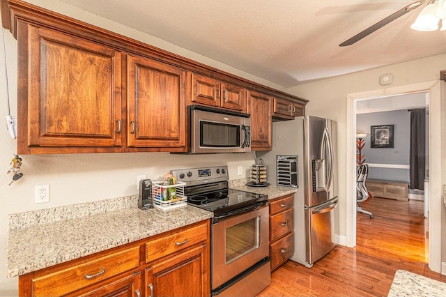 kitchen featuring light wood finished floors, ceiling fan, appliances with stainless steel finishes, and brown cabinets