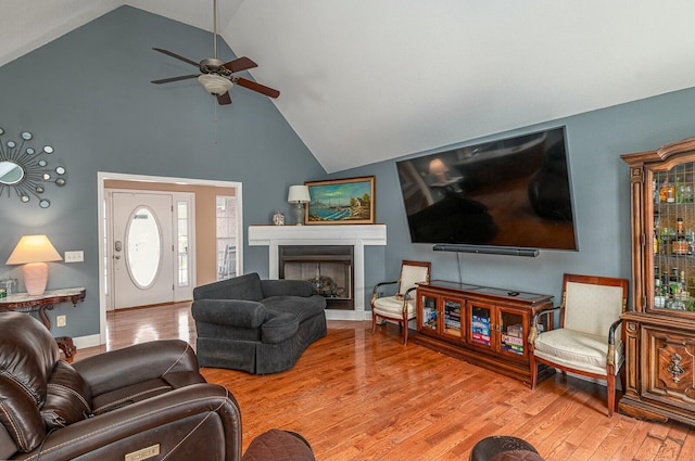 living area featuring baseboards, ceiling fan, wood finished floors, a fireplace, and high vaulted ceiling