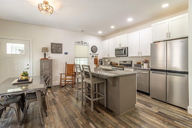 kitchen featuring a center island with sink, dark wood-style floors, appliances with stainless steel finishes, light stone counters, and a sink