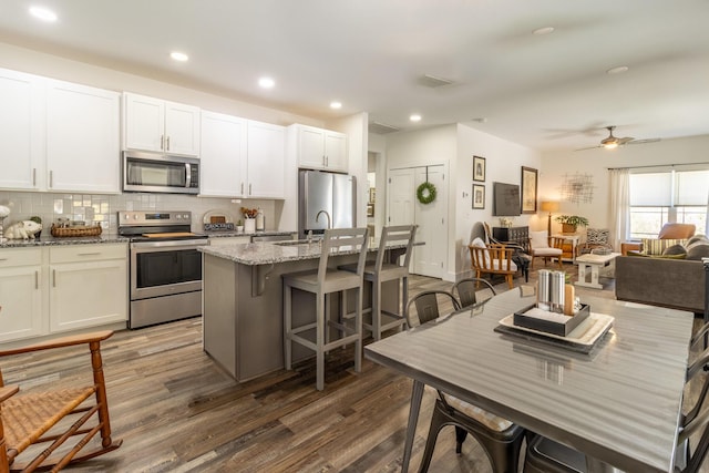 kitchen with stainless steel appliances, a center island with sink, light stone counters, and decorative backsplash