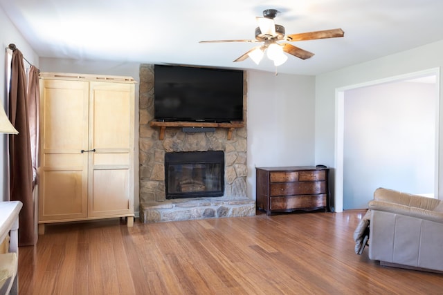 living room featuring a ceiling fan, wood finished floors, and a stone fireplace