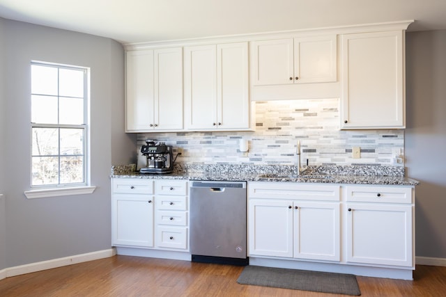 kitchen featuring stainless steel dishwasher, a sink, light stone counters, and tasteful backsplash