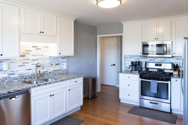 kitchen with white cabinets, light stone counters, dark wood-style flooring, stainless steel appliances, and a sink