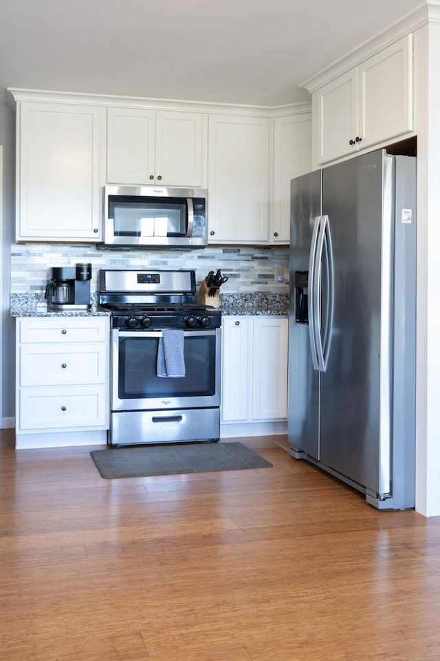 kitchen with appliances with stainless steel finishes, white cabinetry, light wood-style floors, and tasteful backsplash