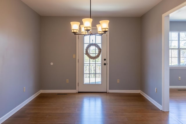 doorway to outside featuring a notable chandelier, dark wood-style flooring, visible vents, and baseboards