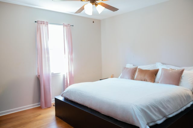 bedroom with a ceiling fan, baseboards, multiple windows, and light wood finished floors