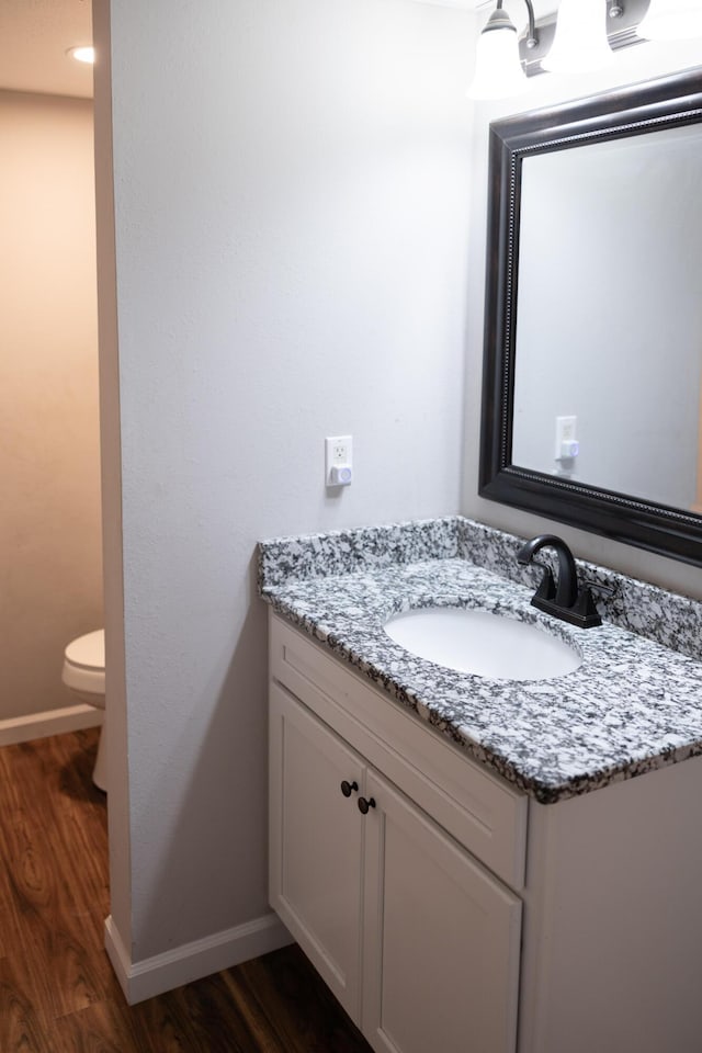 bathroom with toilet, wood finished floors, vanity, and baseboards