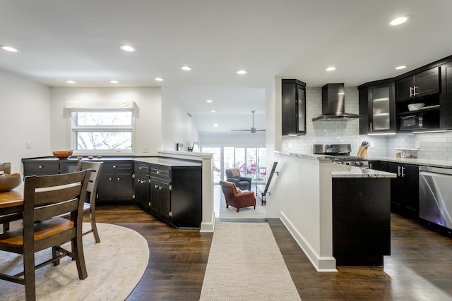 kitchen with wall chimney range hood, decorative backsplash, appliances with stainless steel finishes, and dark cabinets