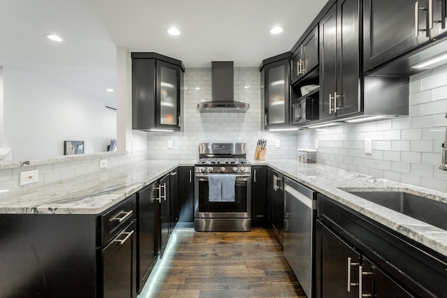 kitchen featuring appliances with stainless steel finishes, light stone countertops, wall chimney range hood, and dark wood-style floors