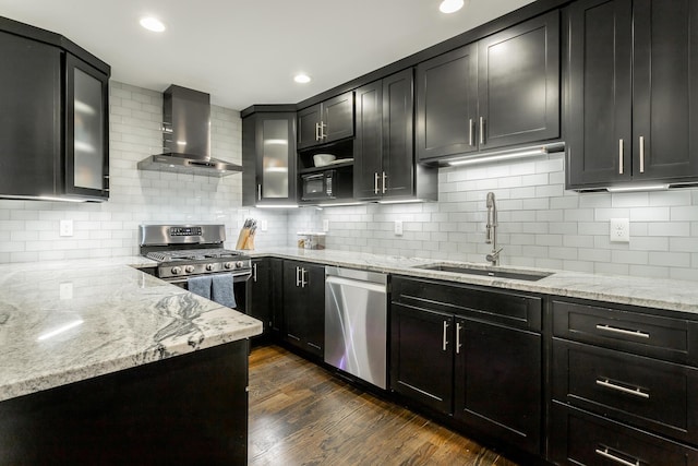 kitchen with wall chimney exhaust hood, appliances with stainless steel finishes, dark wood-style flooring, light stone countertops, and a sink