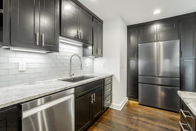 kitchen with dark wood-style floors, stainless steel appliances, backsplash, a sink, and light stone countertops