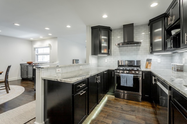 kitchen with light stone counters, wall chimney range hood, a peninsula, dark cabinetry, and stainless steel gas range oven