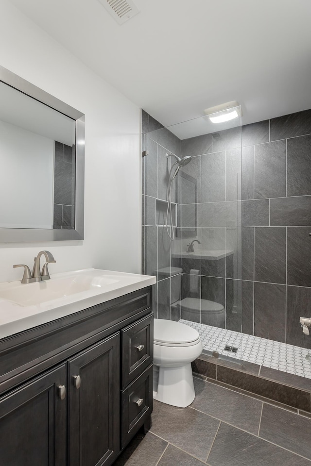 bathroom featuring toilet, visible vents, vanity, tiled shower, and tile patterned floors