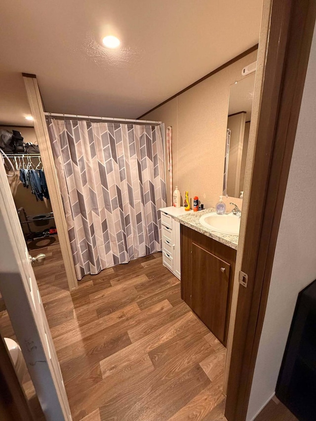 bathroom with a shower with shower curtain, wood finished floors, vanity, a spacious closet, and ornamental molding