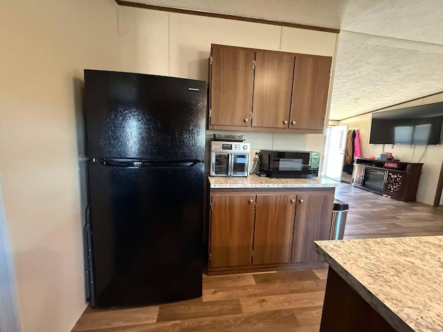 kitchen featuring a textured ceiling, light countertops, brown cabinets, black appliances, and dark wood finished floors