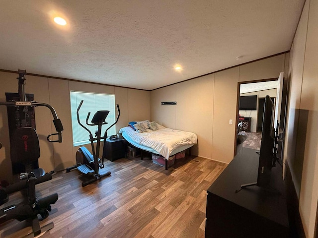 bedroom featuring crown molding, a textured ceiling, a decorative wall, and wood finished floors