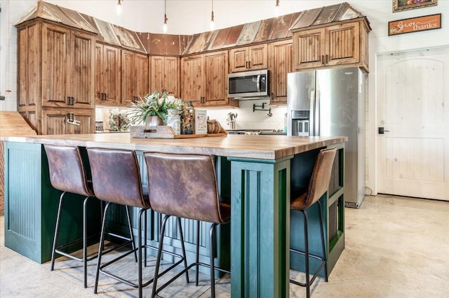 kitchen featuring concrete floors, wood counters, appliances with stainless steel finishes, and a kitchen breakfast bar