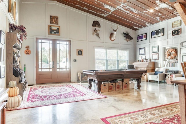 interior space featuring french doors, a decorative wall, high vaulted ceiling, concrete flooring, and billiards