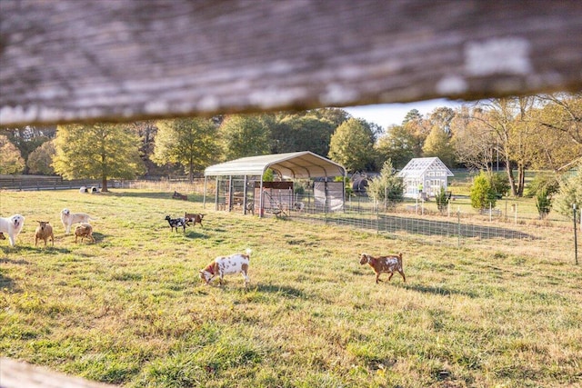 view of yard featuring a carport, a rural view, an outdoor structure, and fence