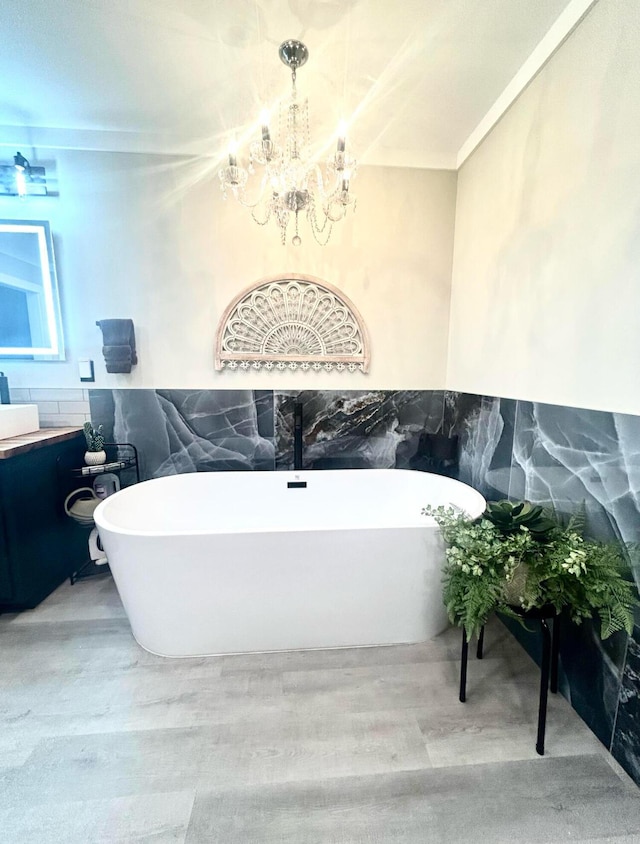 full bath featuring a freestanding bath, wood finished floors, vanity, and a chandelier