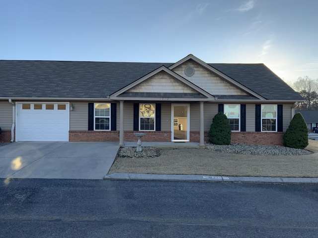 view of front of home featuring a garage, concrete driveway, brick siding, and roof with shingles