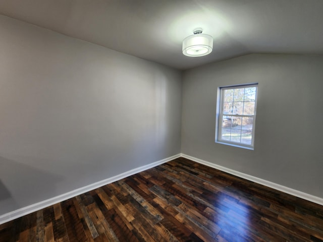 spare room with dark wood-type flooring, lofted ceiling, and baseboards