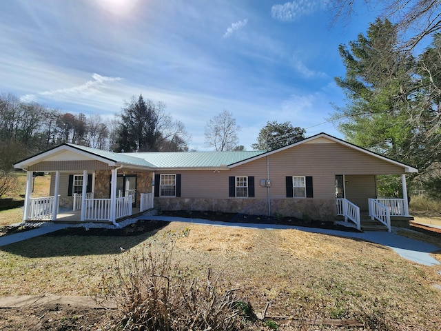 ranch-style house featuring covered porch, stone siding, a front lawn, and metal roof