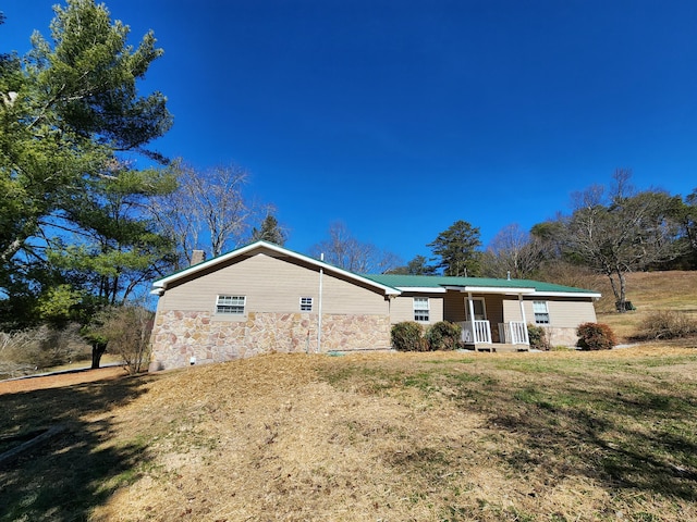 rear view of property featuring stone siding, covered porch, a yard, and metal roof