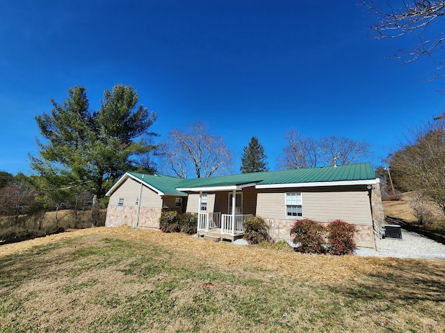 single story home with metal roof, cooling unit, covered porch, stone siding, and a front lawn