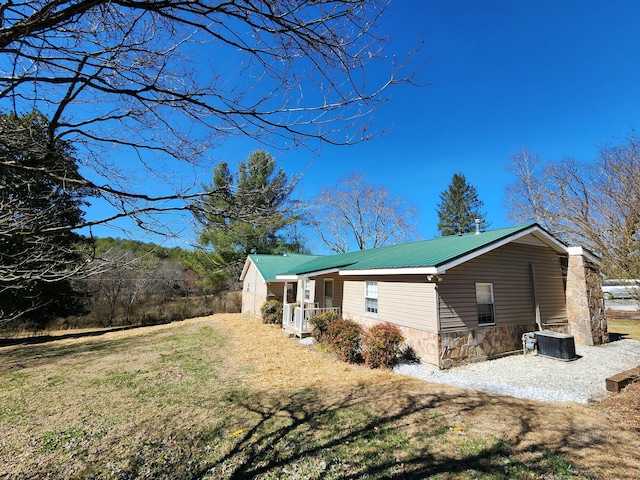 view of property exterior with stone siding, central AC, a yard, and metal roof