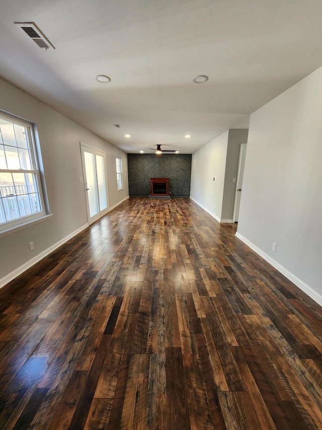 unfurnished living room with visible vents, dark wood-type flooring, a ceiling fan, a large fireplace, and baseboards