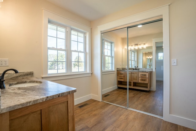 bathroom featuring wood finished floors, two vanities, a sink, visible vents, and baseboards