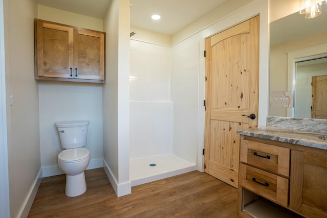 bathroom with toilet, wood finished floors, vanity, baseboards, and tiled shower