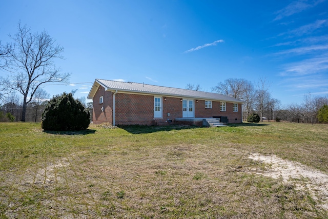 view of front of property featuring french doors, brick siding, metal roof, and a front lawn