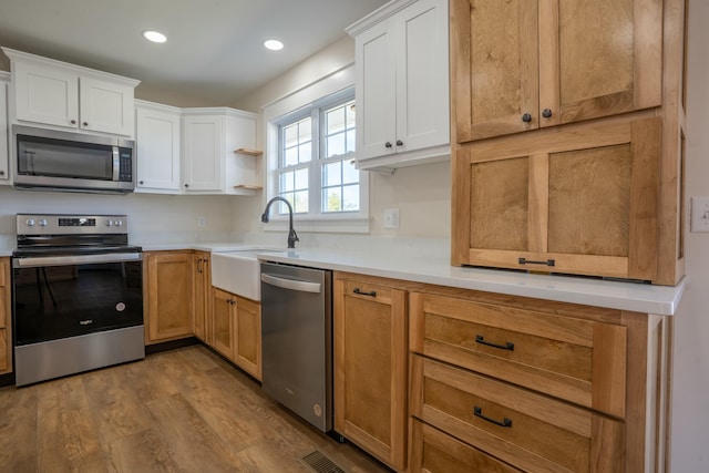 kitchen featuring stainless steel appliances, a sink, wood finished floors, white cabinetry, and light countertops